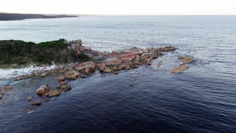 Órbita-Aérea-Suave-Oleaje-Del-Océano-Sobre-Rocas-Rojas,-Bahía-De-Fuegos,-Tasmania