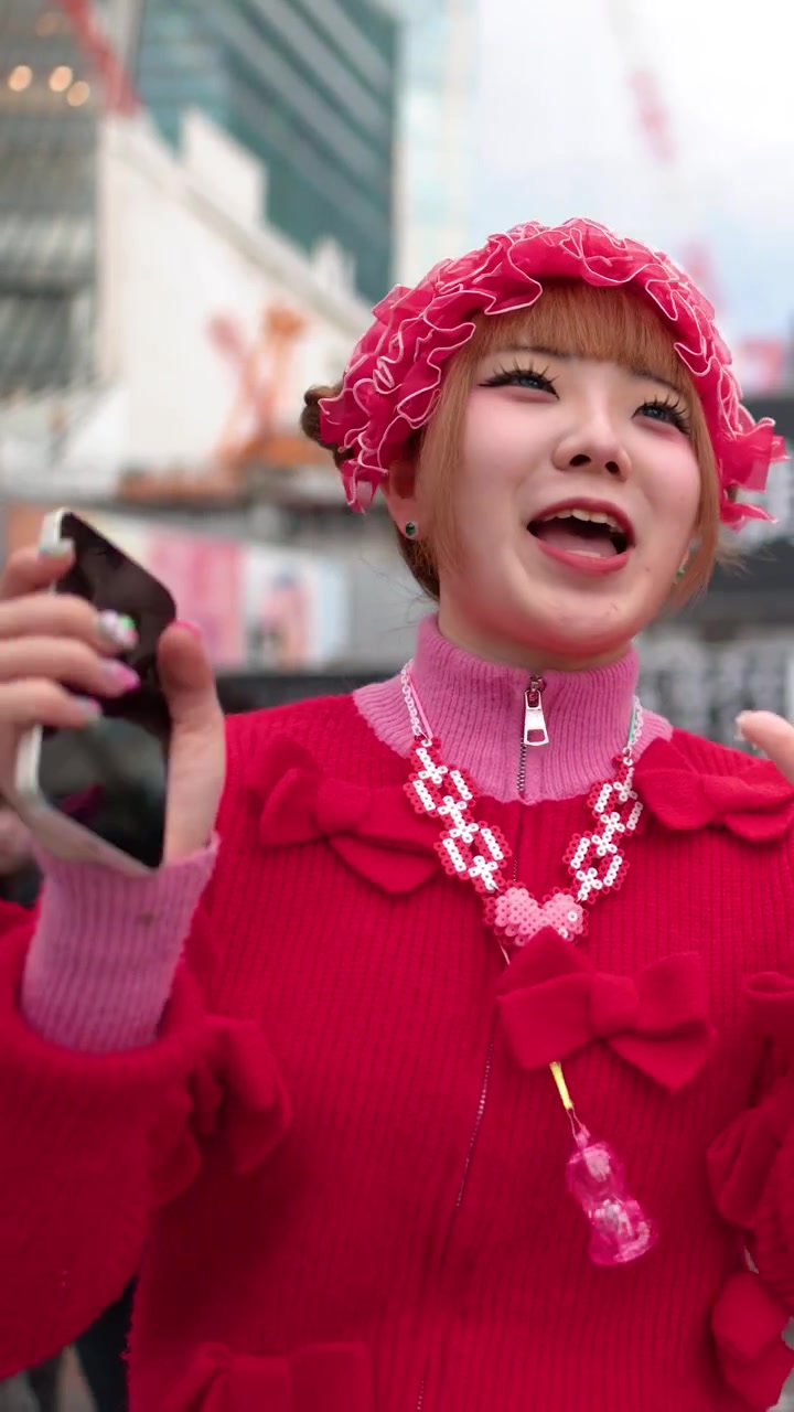 En ung kvinne iført livlig rosa decora-mote roper og smiler i travle Shibuya, Tokyo.
