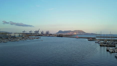 drone aéreo hacia adelante disparado sobre el puerto de algeciras, españa terminal de grúa al amanecer