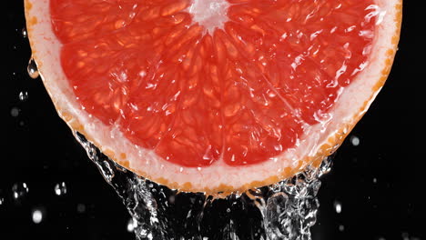 slice of grapefruit and water splashing on the black background in slow motion