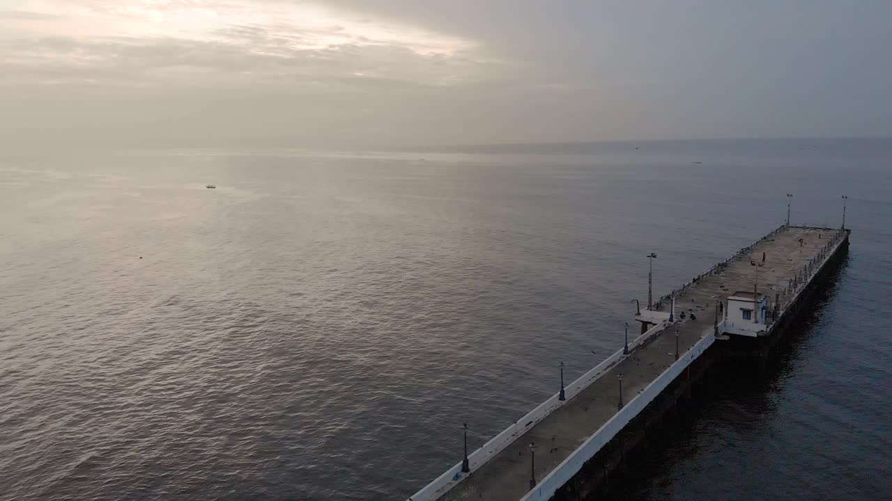 toma aérea de 4k de un muelle del puerto de envío en un amanecer con nubes monzónicas cubiertas cerca de la playa de roca disparada con un dron, pondicherry, india
