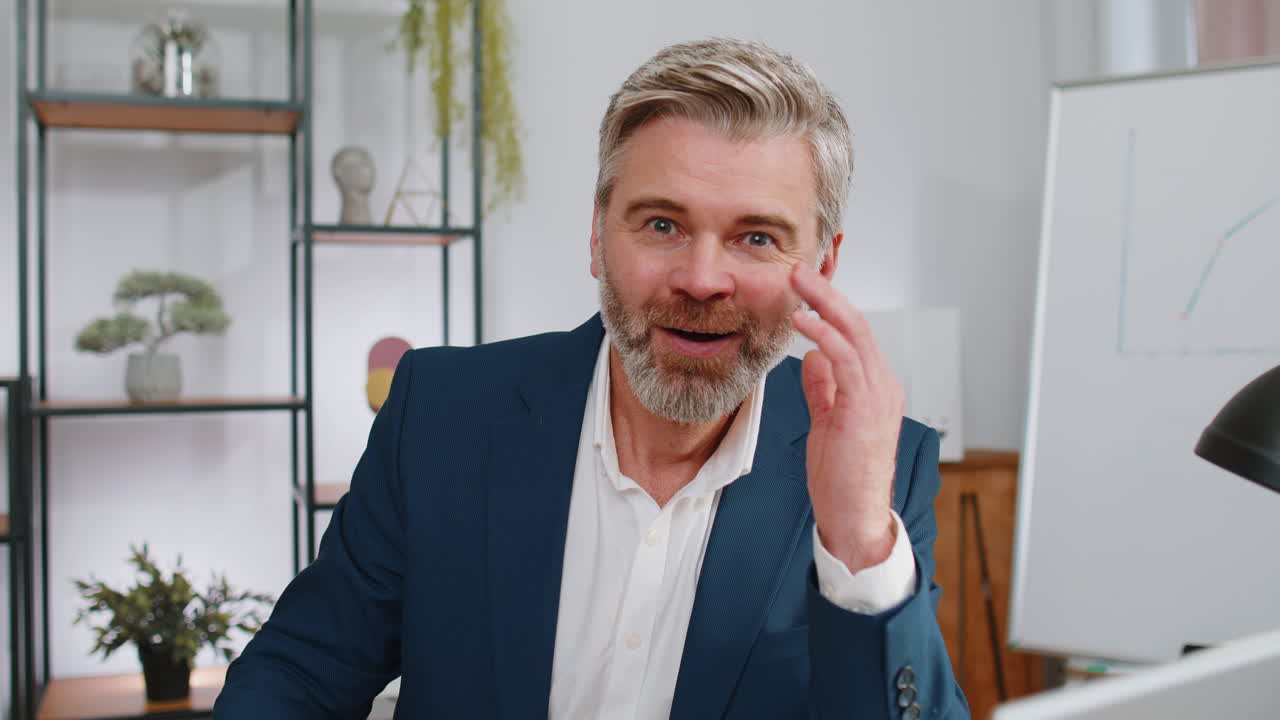 Selvsikker, glad, moden forretningsmann med briller som ser på kameraet med smil på hjemmekontoret