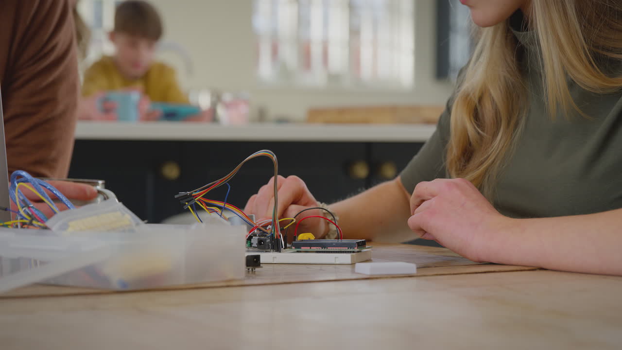 padre ayudando a su hija adolescente con un proyecto de electrónica sentado en la mesa de la cocina en casa con una computadora portátil - filmado en cámara lenta