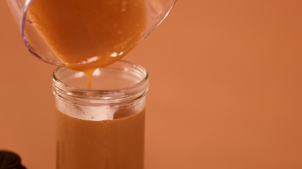 Denso frullato al cioccolato versato delicatamente da un frullatore in un barattolo di vetro, illuminazione calda, telecamera statica