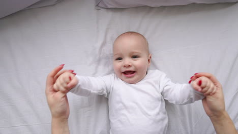 a child in a white t-shirt lying on a white bed looking at the camera and laughing in slow motion, top view