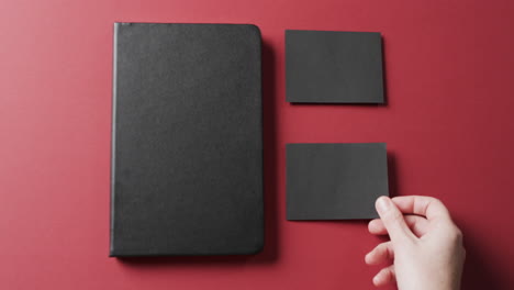 video de una mujer caucásica poniendo tarjetas de papel negro con espacio de copia y cuaderno en fondo rojo