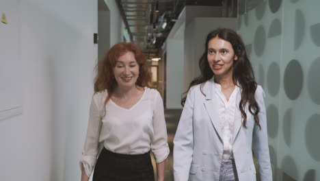 two young businesswomen walking through the corridors of an office building discussing company matters