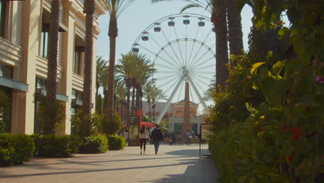 an outdoor shopping center in southern california, featuring a giant ferris wheel attraction, with only a few patreons during the covid-19 pandemic