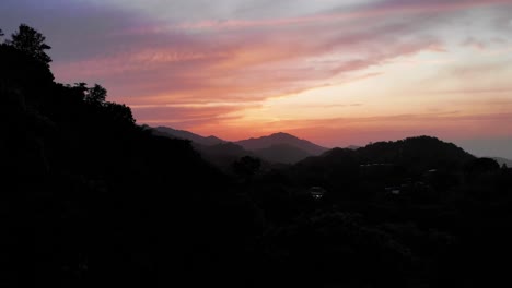 Aerial-rising-out-of-dark-jungle-revealing-stunning-sunset-over-silhouette-mountain-peaks-in-Amazon