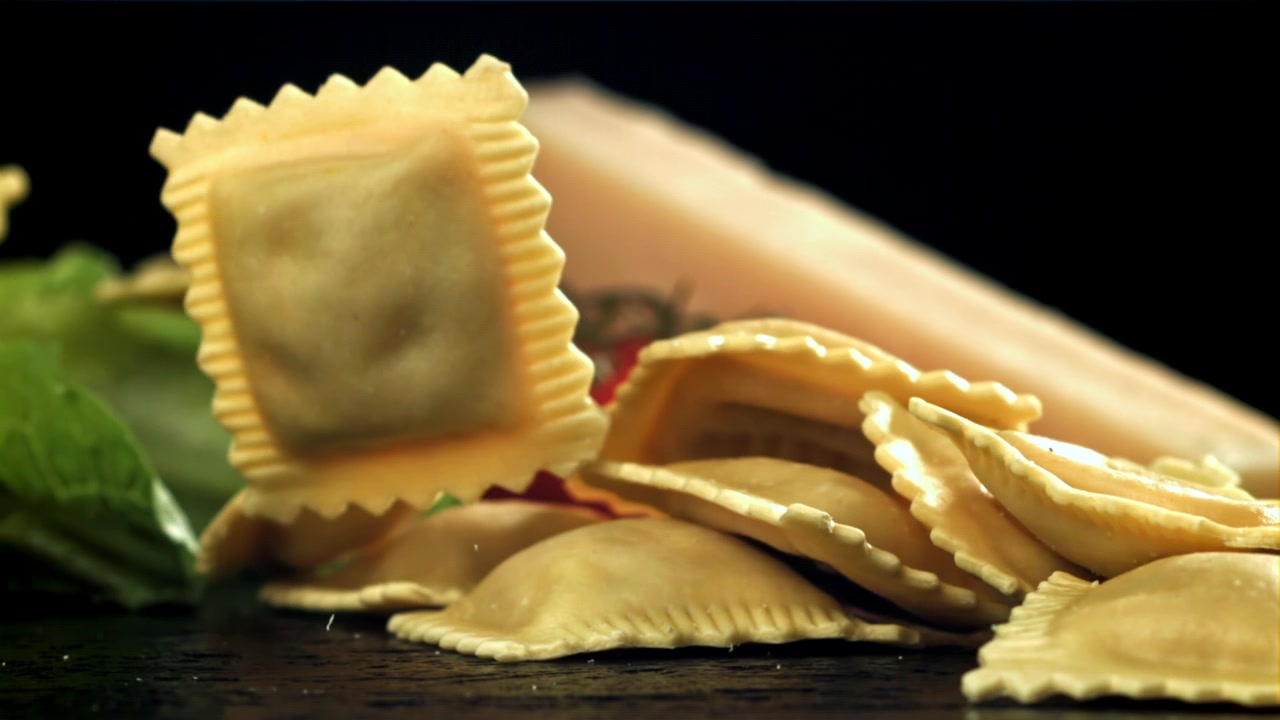 Čerstvé ravioli padající ve zpomaleném záběru s italskými ingrediencemi.