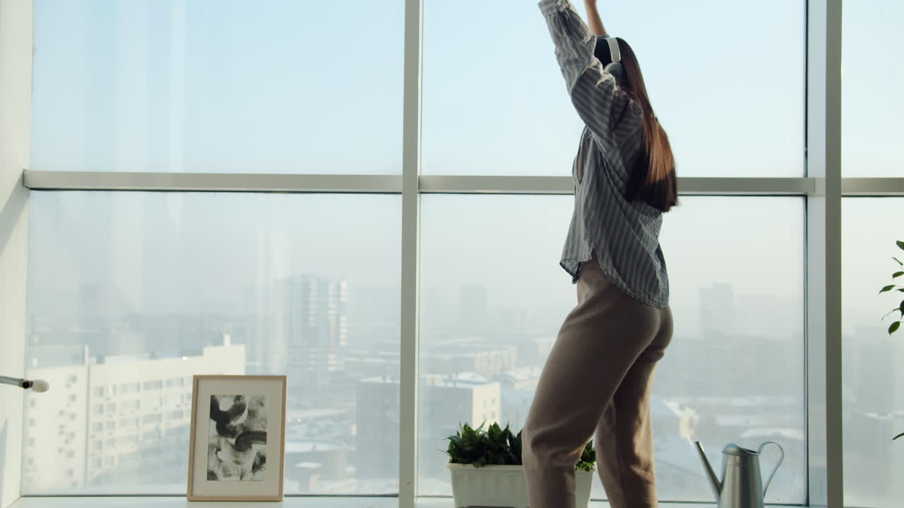 Woman dancing by the window in her cozy apartment