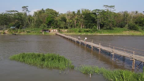 people crossing a bamboo bridge over a river in a tropical forest