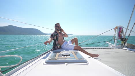 4k caucasian man talking on phone for corporate business while catamaran boat sailing on summer vacation.