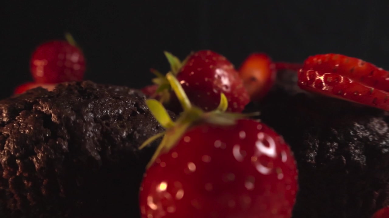 Carrellata ravvicinata che rivela deliziosi muffin al cioccolato fatti in casa, o brownies, decorati con fragole fresche e mature su uno sfondo scuro, creando una scena di dessert da acquolina in bocca