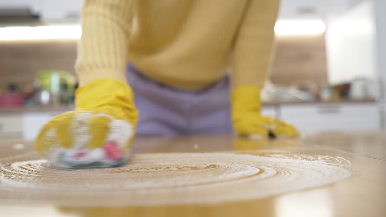 家庭内で、保護手袋を着用した女性がスポンジと泡でテーブルを掃除している様子。春の大掃除、衛生、ホームケア、家事代行のイメージ。