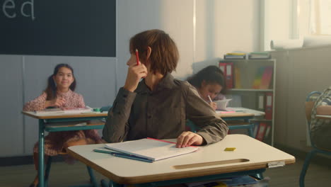 Boy-sitting-at-desks-in-school-class.-Pensive-schoolboy-holding-pencil-in-hand