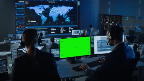 pantalla verde maqueta horizontal en la pantalla de la computadora utilizada por el controlador en el centro de control de vigilancia con seguimiento de mapa global en una gran pantalla digital. los empleados de la sala de monitoreo analizan grandes datos.