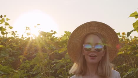 Schöne-Junge-Frau-Mit-Strohhut,-Sonnenbrille-Und-Weißem-Kleid-Im-Landhausstil,-Die-Bei-Sonnenuntergang-Im-Sonnenblumenfeld-Lächelt-Und-Tanzt