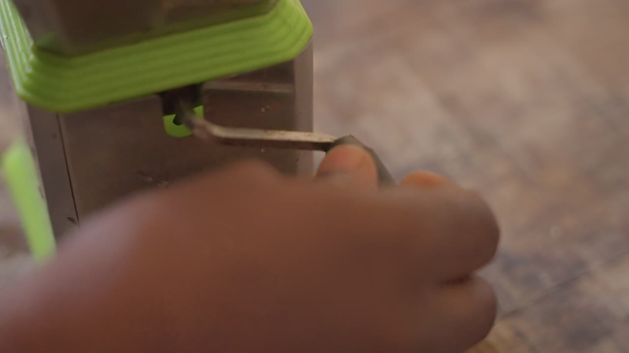 Closeup black adult hands adjusting bit on small manual drill atop rustic bench, calm precision carpentry scene, artisan focus on detail and finish, gentle motion and fine shavings