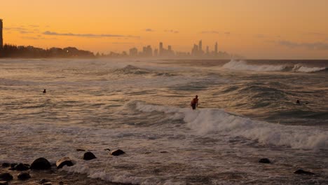 surfers at sunset with city skyline in background