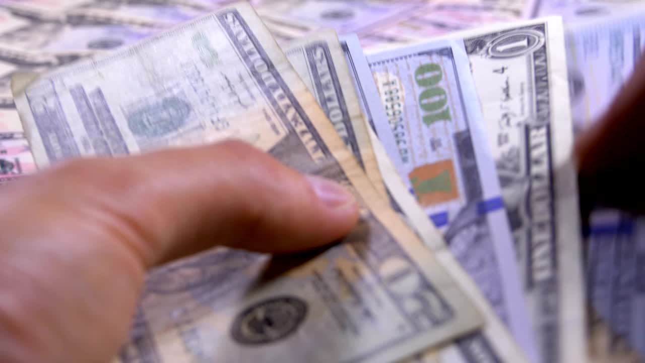 las manos de los hombres sostienen un montón de dólares estadounidenses contra el fondo de dinero giratorio
