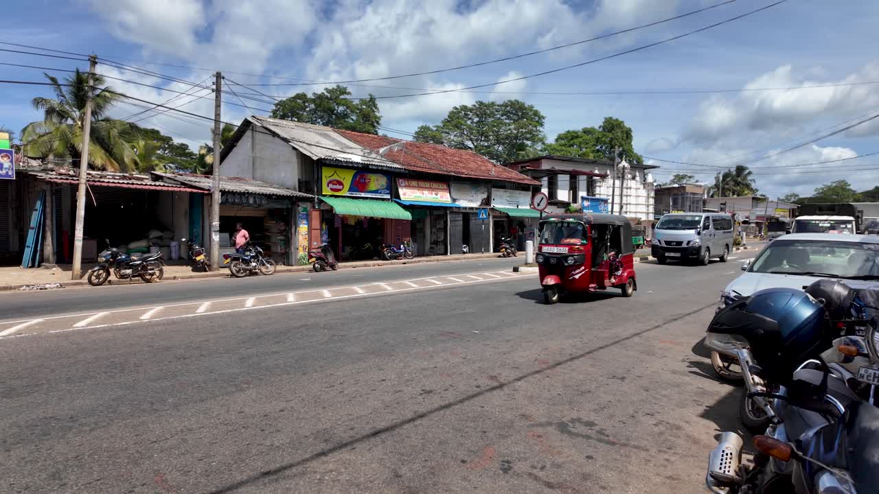Vibrant street view in a Sri Lankan town featuring a red tuk tuk amidst local traffic. A glimpse into everyday life and culture in Sri Lanka.
