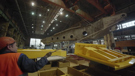 industrial worker operating crane to move large metal component