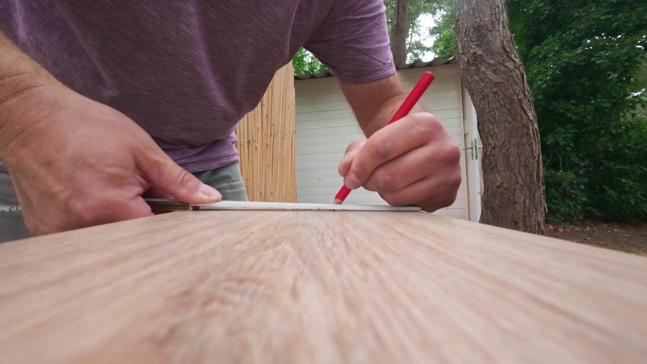 Detailed perspective of an installer measuring and marking white oak laminate floor planks. Focus on precision work and material preparation for a professional flooring installation.