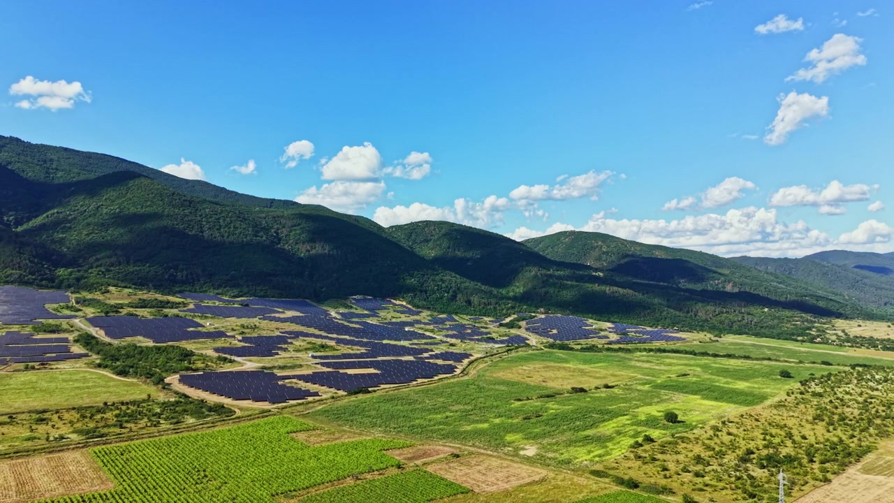 昼間、澄み切った空の下、山に近い田園地帯に広がるソーラーパネル畑