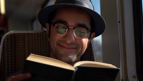 man smiling while reading a book on a train