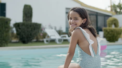 side view of girl sitting by swimming pool on warm summer day.