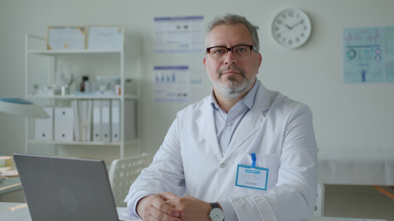 Retrato de um médico de meia-idade usando um laptop no trabalho em uma clínica
