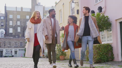 grupo multicultural de amigos abrazados mientras caminan por la calle empedrada de mews en visita a la ciudad en otoño o invierno - filmado en cámara lenta