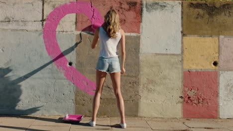 artista de graffiti mujer pintando forma de corazón en la pared con pintura rosa rebelde joven mujer disfrutando de la expresión artística con paz y amor concepto de arte callejero urbano 4k