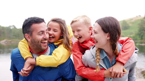 Parents-piggybacking-their-children-and-laughing-to-camera-in-the-countryside,-close-up,-Lake-District,-UK