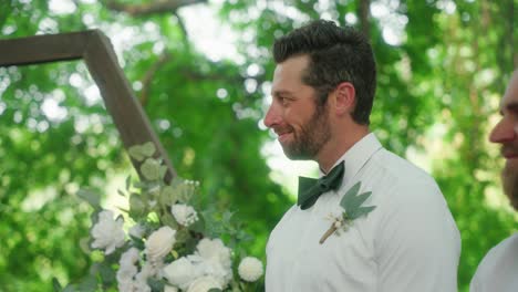 best man smiles proudly at bride and groom under forest arch