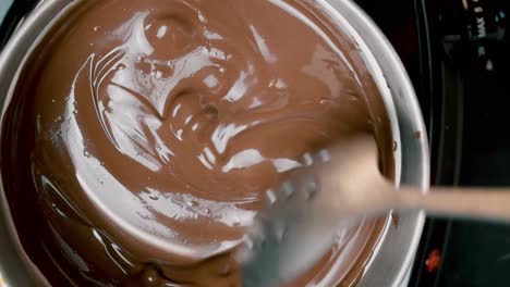 top view into melting pot of milk chocolate candy rounds being stirred with spoon as they completely melt