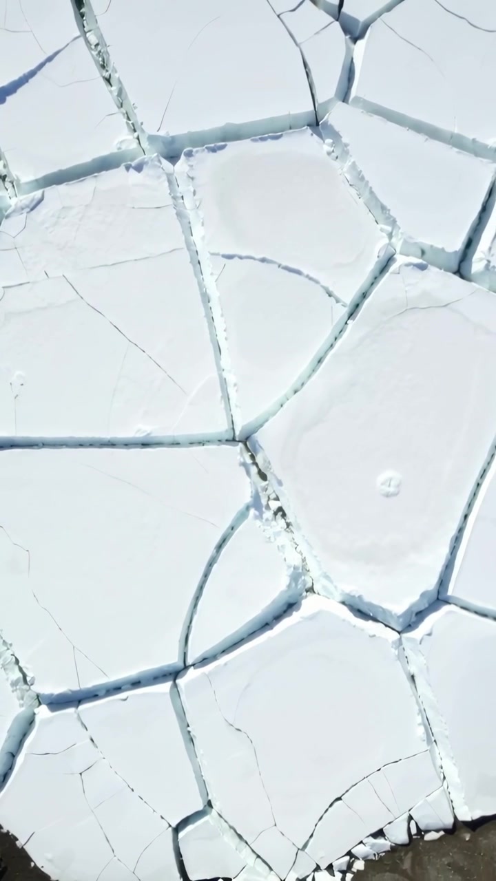 Vertical video: Drone panning over polygonal plates, revealing narrow cracks and dark shore