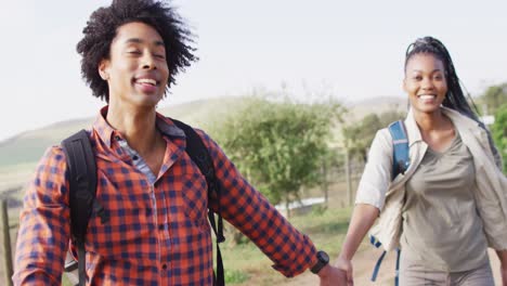 Glückliches-Afroamerikanisches-Paar-Mit-Rucksäcken,-Gemeinsames-Wandern-An-Einem-Sonnigen-Tag,-Zeitlupe