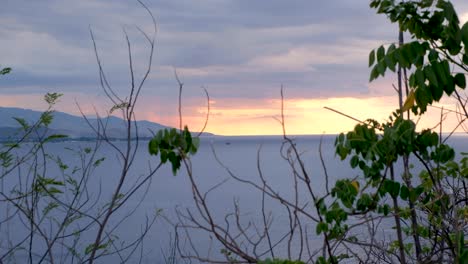 Un-Vistazo-De-Un-Barco-En-La-Distancia-Anclado-En-Una-Impresionante-Puesta-De-Sol-Nublada-De-Color-Rosa-Y-Naranja-En-Una-Remota-Isla-Tropical