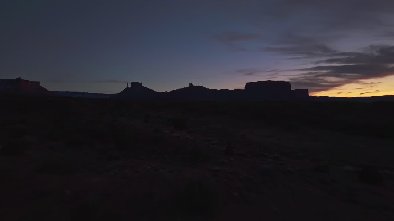 Drone vast Moab desert at twilight, glowing red sandstone cliffs and deep valleys below, silhouette against glowing sky