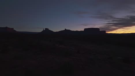drone vast moab desert at twilight, glowing red sandstone cliffs and deep valleys below, silhouette against glowing sky