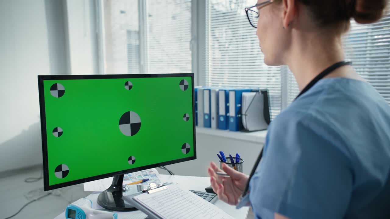 el trabajador sanitario consulta al paciente en línea a través de una computadora con pantalla de tecla cromada, la doctora en uniforme azul con estetoscopio habla y hace gestos en el lugar de trabajo