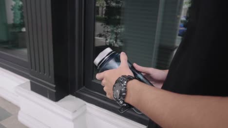 Man-holding-water-bottle-while-wearing-a-black-watch-and-walking-down-the-street-along-a-corridor-in-slow-motion