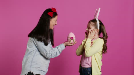 lovely mother surprising her daughter with a cute pink egg for easter