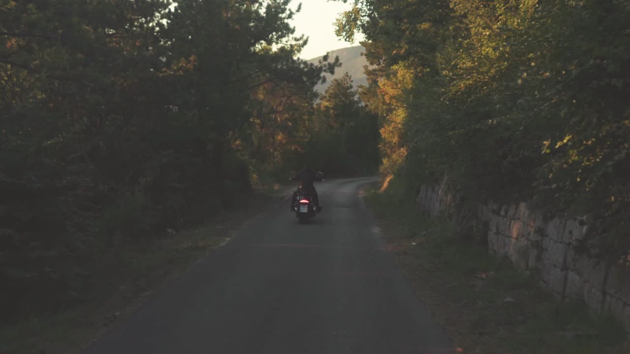 해가 지는 동안 휘어지는 숲길 에 있는 오토바이 운전자