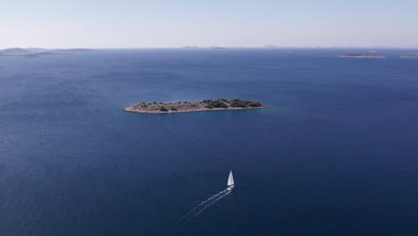 Yate-De-Vela-En-Un-Mar-Azul-Tranquilo-Con-Una-Remota-Isla-Deshabitada,-Antena