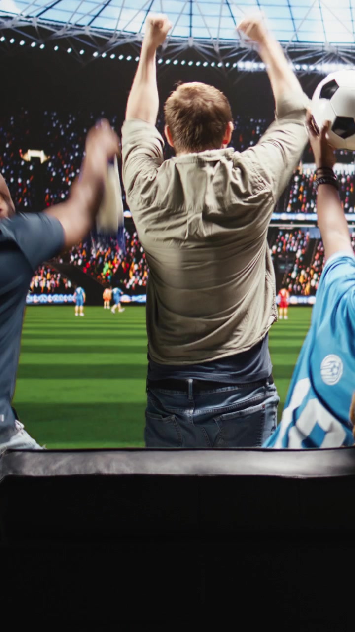 Video vertical. Aficionados al fútbol celebran un gol en casa, viendo el partido en una transmisión de TV interactiva.