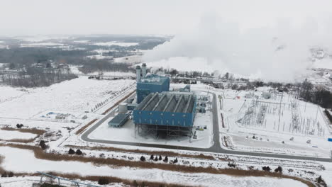 an industrial facility in a snowy landscape with steam rising, winter, aerial view