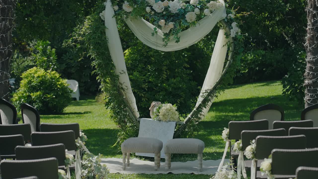 Romantic outdoor wedding ceremony setup with chairs and floral arch in a lush garden setting